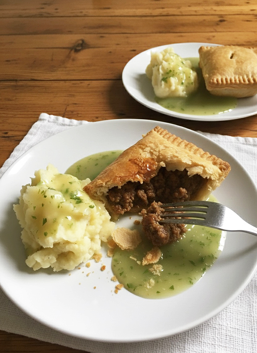 Traditional British pie and mash with minced beef pies, creamy mashed potatoes, and parsley liquor sauce, a classic UK comfort food