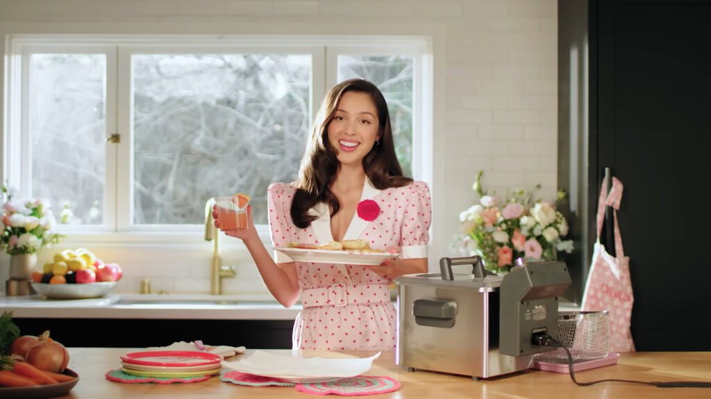 Olivia Rodrigo holding a plate of homemade lumpia alongside a calamansi Paloma cocktail, highlighting her Filipino recipes.