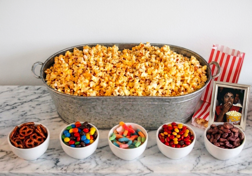 Self-serve popcorn station with a large tub of popcorn and bowls of assorted toppings, set up for a Michael movie night inspired by Michael Jackson’s legacy and “Thriller” popcorn meme.