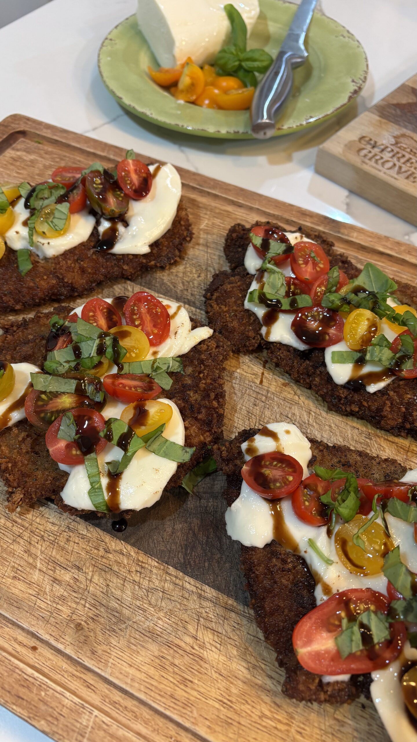 Caprese chicken cutlets topped with melted mozzarella, cherry tomatoes, and fresh basil on a plate